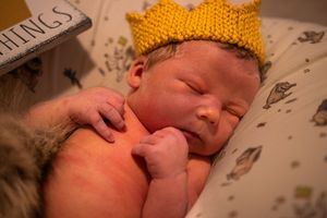 A sleeping newborn baby wearing a bright yellow knitted crown hat rests peacefully.