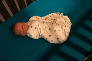 A sleeping baby wrapped in a white patterned onesie rests on a teal colored surface.
