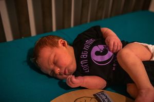A baby in a dark t-shirt sleeps soundly on teal-colored bedding.