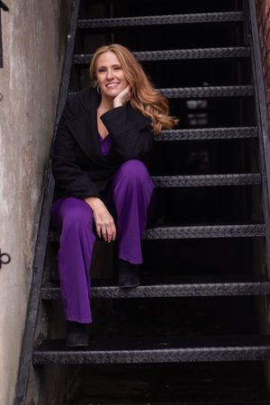 A woman in a purple dress poses on dark metal stairs in an artistic maternity photoshoot.