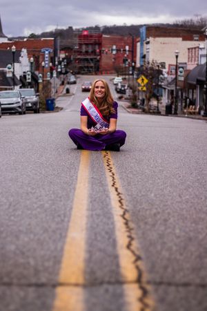 Person in purple outfit poses playfully on yellow road lines in small town street.