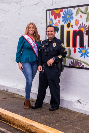 People pose together against white wall with colorful flower mural in small town setting.