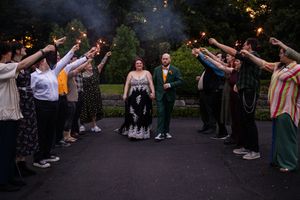 Wedding guests forming an arch tunnel with raised arms outdoors at dusk.