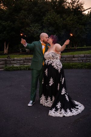 A romantic dance dip pose captured at sunset on a dark paved surface near stone walls and trees.