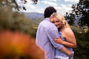 Couple sharing an intimate embrace outdoors with mountain landscape and autumn foliage in the background.