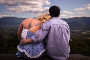 Couple in romantic embrace overlooking scenic mountain landscape at sunset.