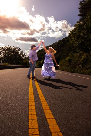 A couple dances together on an empty road at sunset, casting long shadows across the double yellow lines.