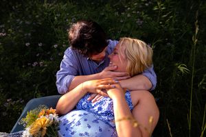 A couple shares an intimate moment while resting in a sunlit meadow.