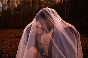 A figure draped in a delicate pink veil stands in an autumn forest setting with fallen leaves on the ground.