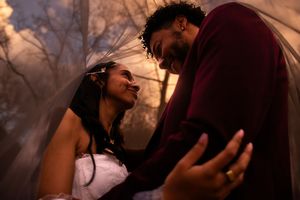 A couple embraces in a romantic sunset silhouette against warm autumn trees and glowing sky.