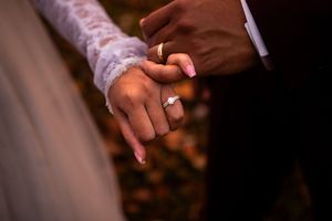 Two hands holding each other in a romantic gesture against a dark background.