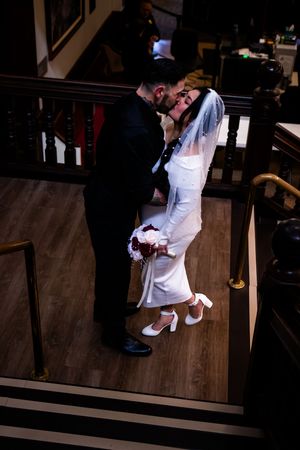 Romantic wedding couple sharing intimate moments on wooden stairs in a dimly lit setting.