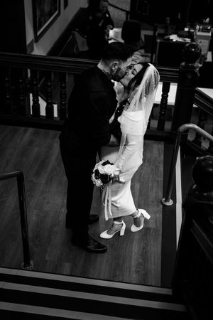 A black and white wedding photograph showing a couple embracing on wooden stairs in a church.
