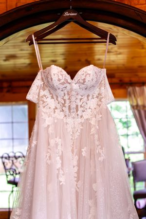 Elegant white lace wedding dresses hanging in a row on wooden hangers under rustic beams.