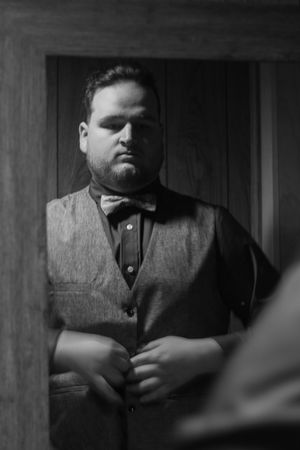 A dramatic black and white sequence showing a person in dark clothing against a wooden wall background.