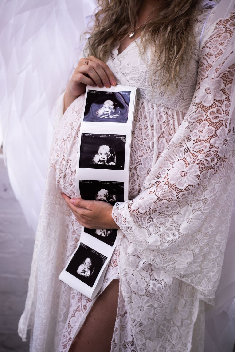 Person in white lace robe holds ultrasound photos in a pregnancy announcement photoshoot series.