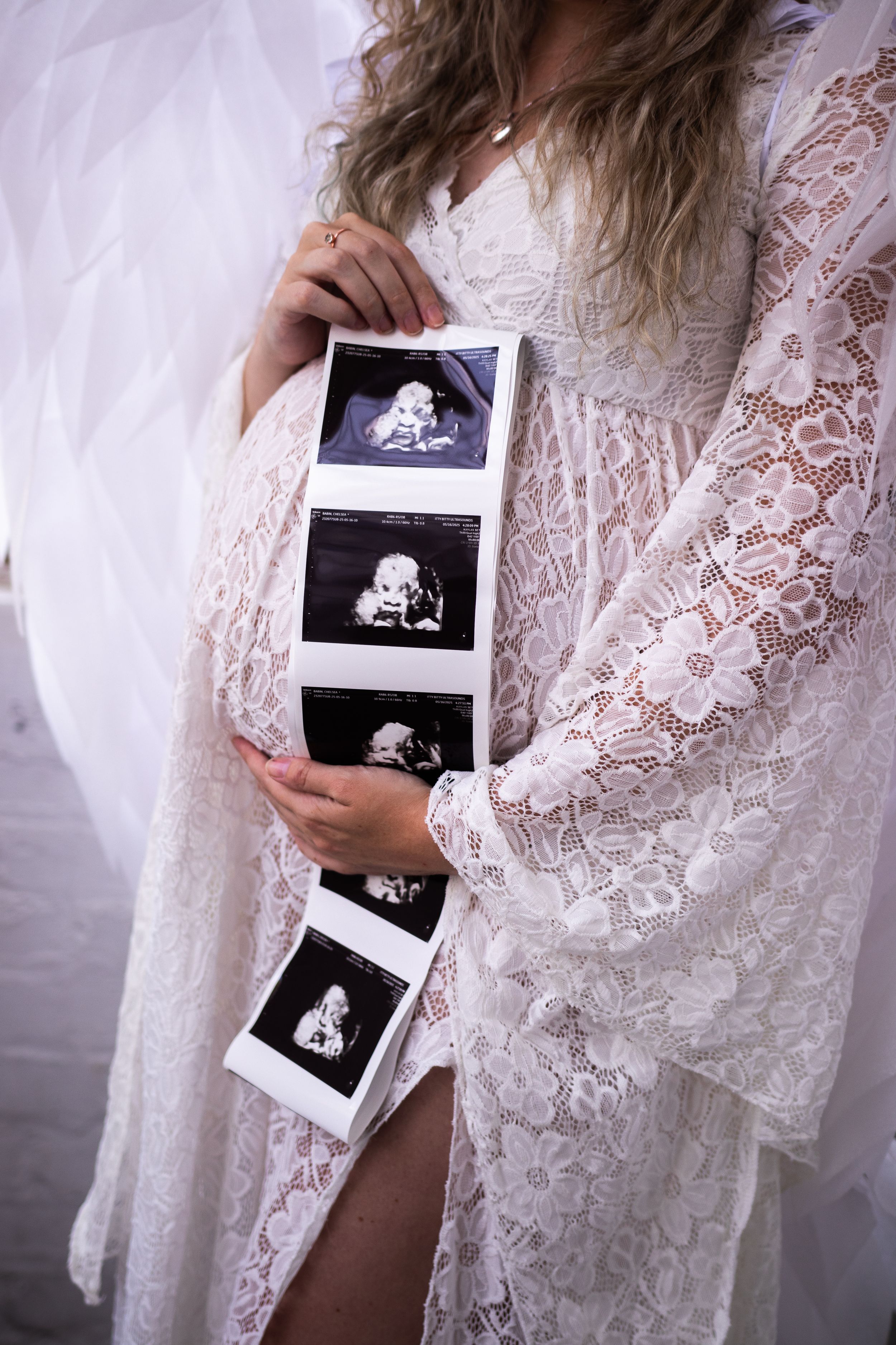 Person in white lace robe holds ultrasound photos in a pregnancy announcement photoshoot series.