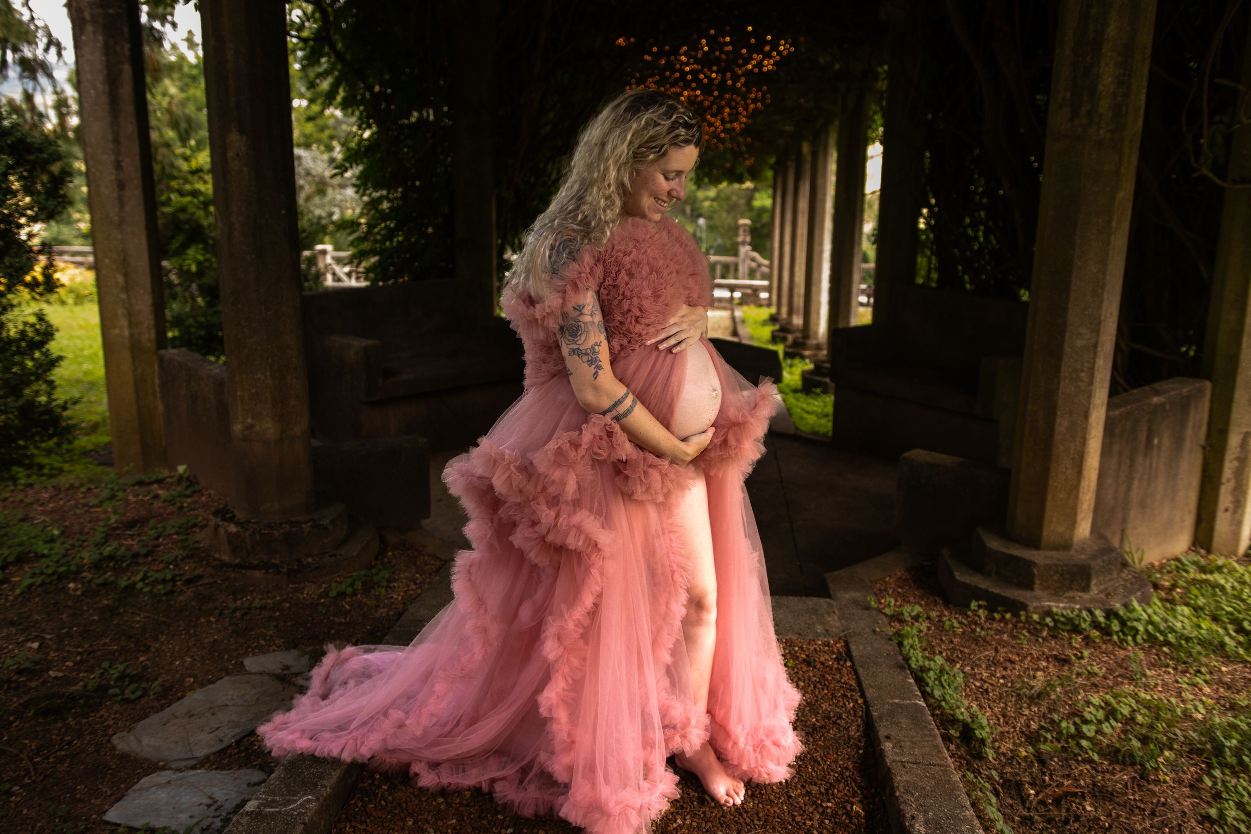 A person in a flowing pink tulle gown twirls gracefully in a wooded outdoor setting.