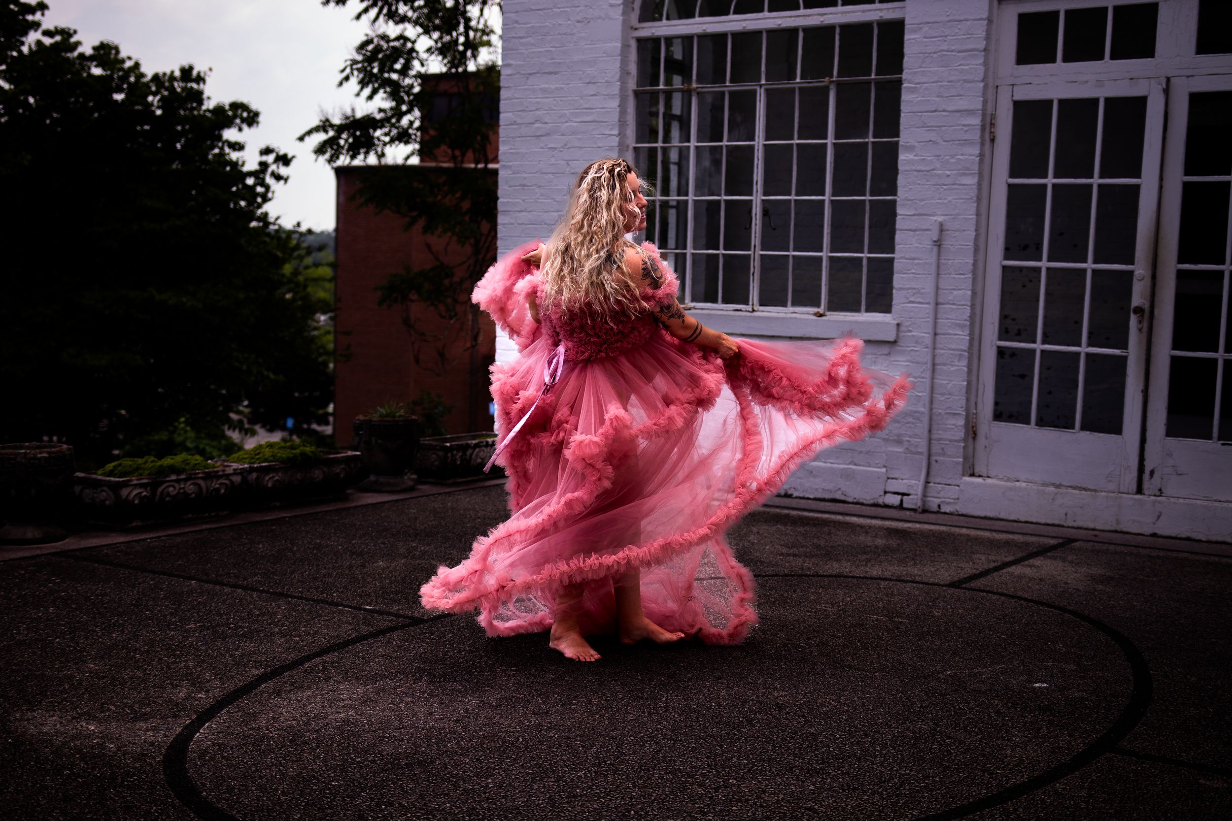 A pink tulle dress swirls dramatically against the backdrop of a white building with windows.