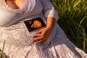 Person in a white lace dress sits gracefully in lush green grass during a sunny outdoor photo session.