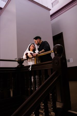 A couple sharing an intimate moment on a vintage wooden staircase in a dimly lit interior setting.