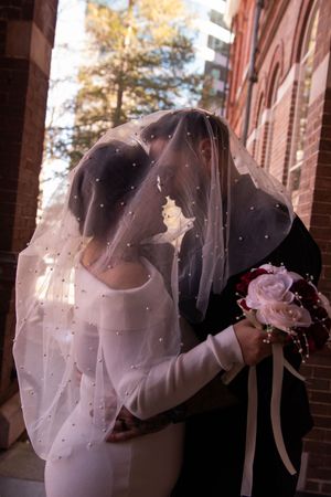 Romantic wedding couple in a dip pose with flowing veil on a brick building porch.