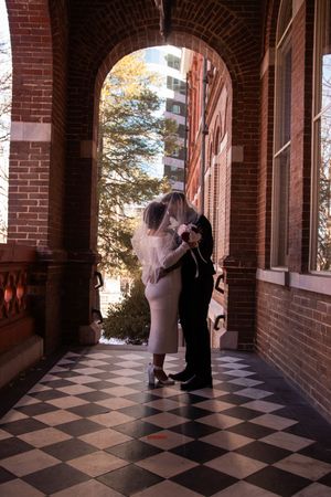 A wedding couple dances in a brick archway with checkered floor tiles creating an elegant architectural frame.