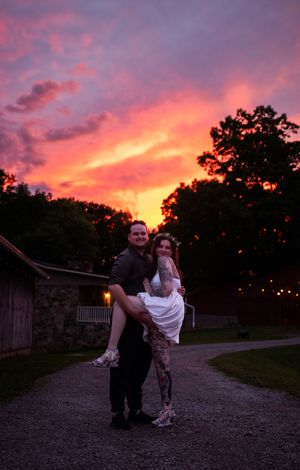 A couple poses romantically on a path at sunset with vibrant pink and orange sky in the background.