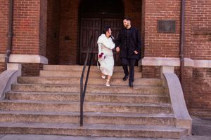 Couple walking along brick building exterior with stone steps and railing.