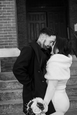Wedding couple embracing outside a brick building in black and white photography.