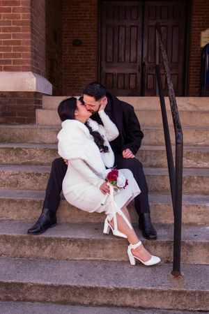 Newlyweds share tender moments while sitting on brick steps in formal wedding attire.