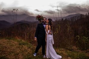 A couple in wedding attire stands in silhouette against dramatic mountain views at sunset.