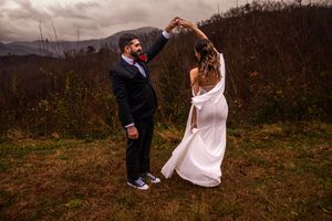 A couple dances together on a hillside during an autumn wedding celebration in the mountains.
