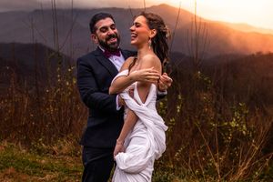 Couple embraces during golden sunset in rustic outdoor setting with tall grass and natural lighting.