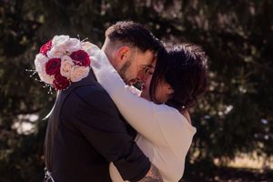 Couple embraces in romantic outdoor setting with red floral accents at sunset.