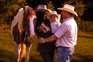People in western attire gather around horses in a golden-lit field during sunset.
