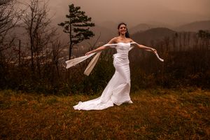 A bride in a flowing white dress poses gracefully across scenic mountain landscapes at sunset.