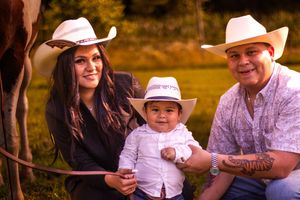 A family in white cowboy hats poses together outdoors during golden hour in a rustic setting.