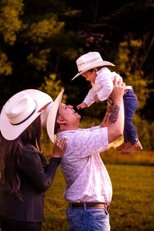 A family shares a joyful moment together outdoors while wearing cowboy hats in warm evening light.
