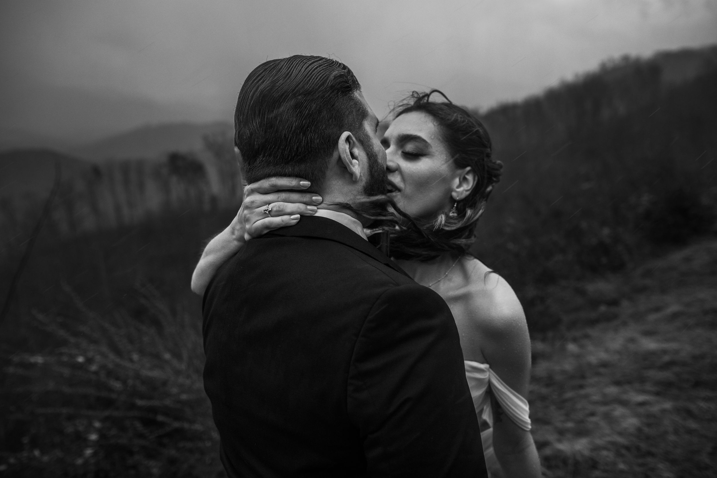A romantic black and white wedding photo of a couple sharing an intimate kiss on a misty mountainside.