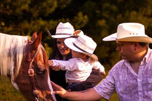 A group of people wearing cowboy hats dance together outdoors during a country western event.
