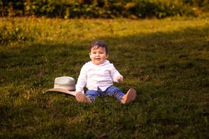 A small child sits on grass in golden sunlight next to a cowboy hat during sunset.