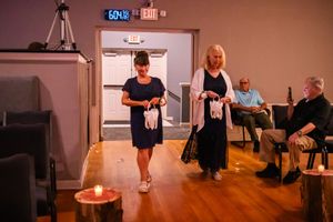 Wedding guests gather around a candlelit cake in a dimly lit reception venue.