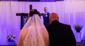 A wedding ceremony venue with purple uplighting and white fabric draping creates an elegant atmosphere.