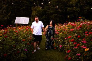A couple dances together in a garden filled with vibrant red flowers during sunset.