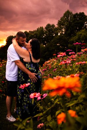 Couple shares tender moment among pink flowers during dramatic sunset.