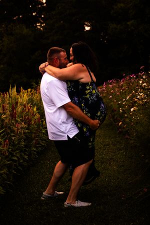 A couple embraces romantically in a garden with blooming flowers at sunset.