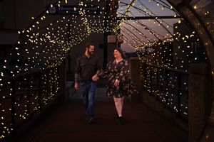 A couple walks through a romantic tunnel illuminated by twinkling string lights creating a magical evening atmosphere.