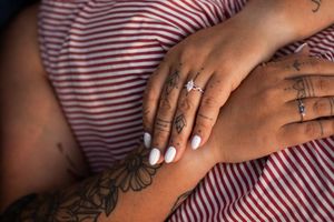 Close-up sequence of hands with white manicured nails and tattoos against pink and white striped fabric.