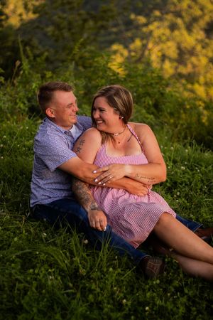 A couple shares a romantic moment lying in green grass during golden hour sunset.